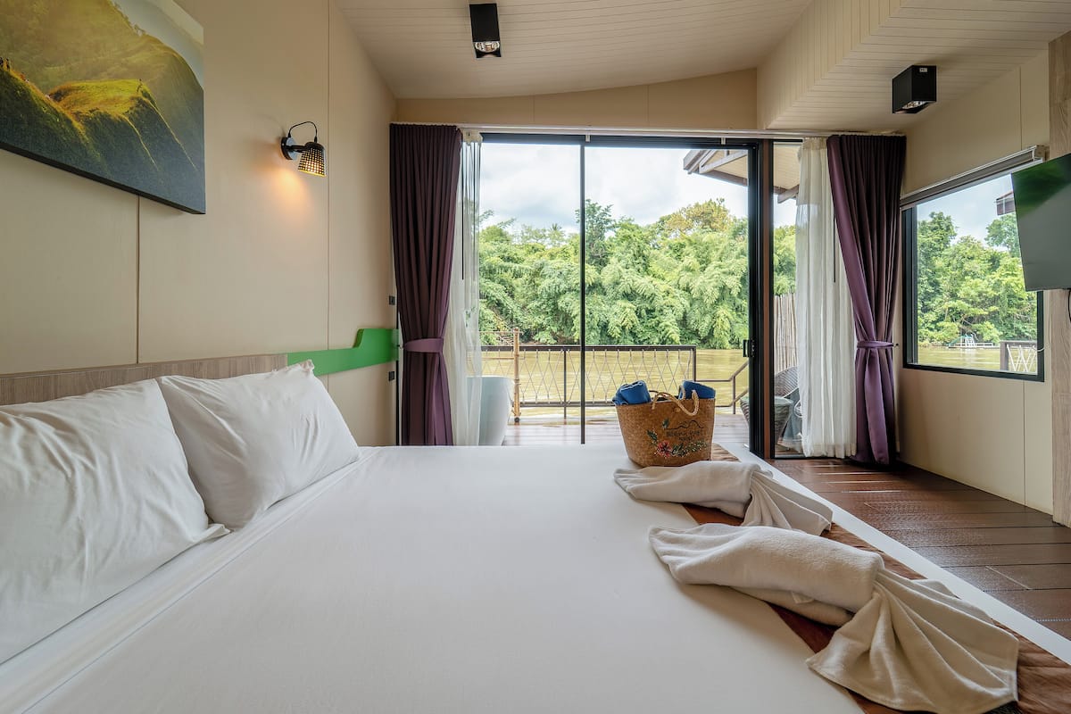 A hotel room with a large bed, a view of the outdoors, a painting on the wall, and a basket on the floor.