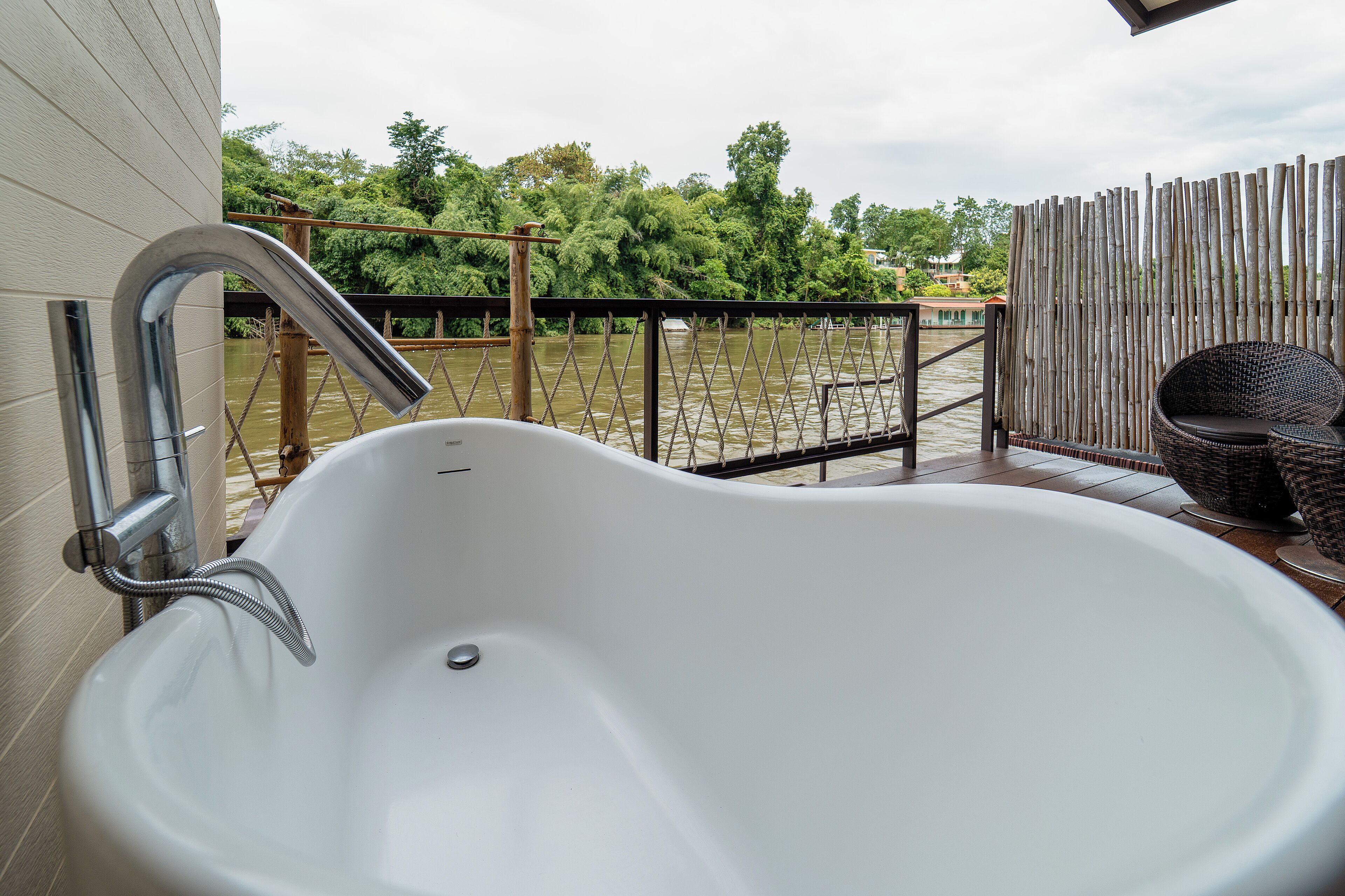 Une baignoire blanche sur un balcon, avec une clôture en bambou et des meubles en osier.