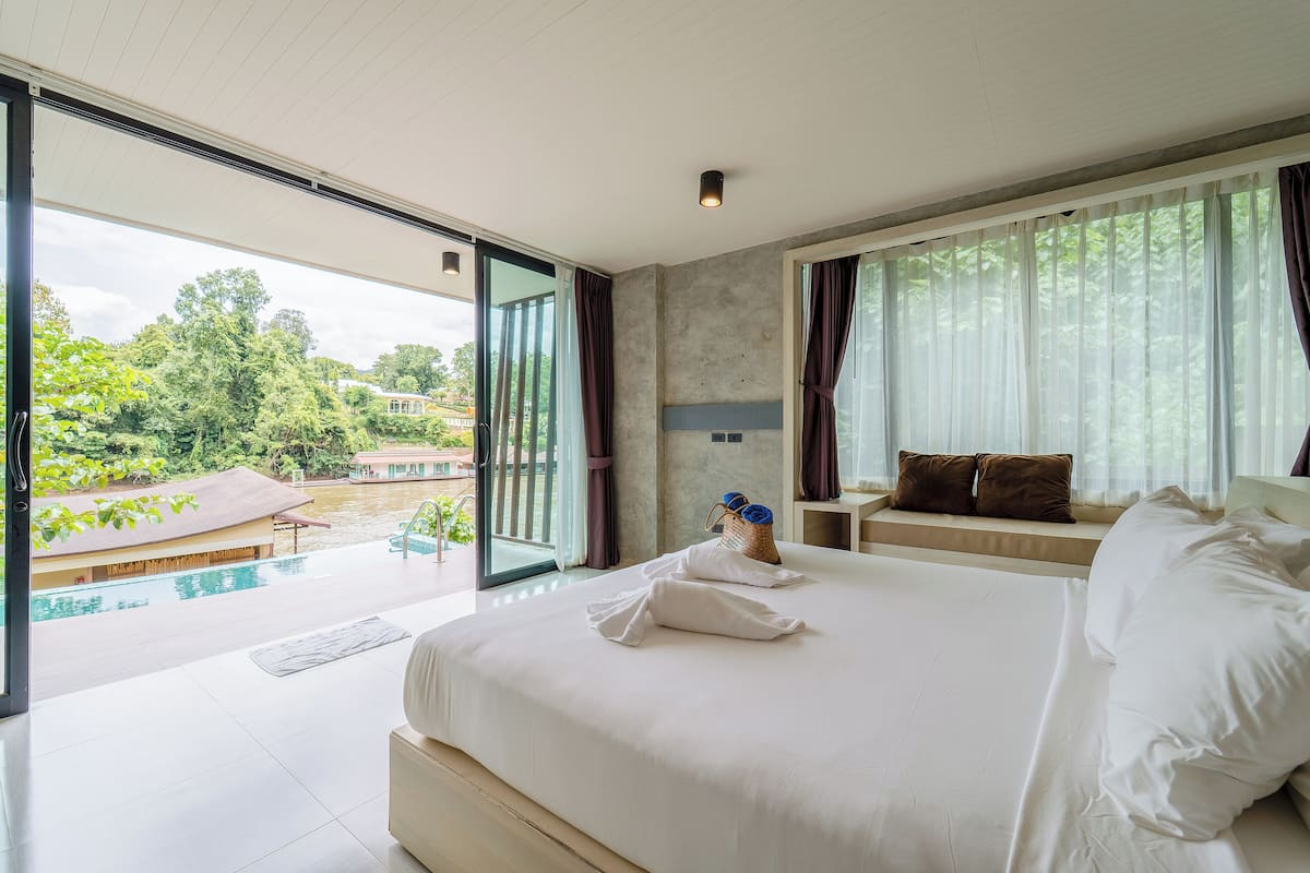 A spacious bedroom with a large bed, a view of a swimming pool, and a balcony.
