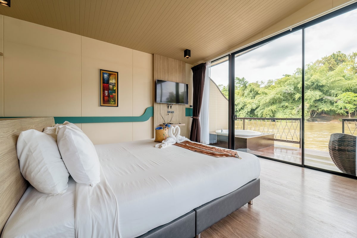 A modern hotel room with a large bed, a flat-screen TV, a painting, and a view of a natural landscape.