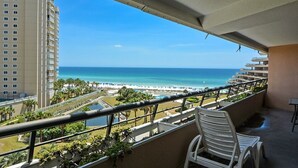 Un balcon avec vue sur l’océan et la plage, une piscine et un fauteuil.