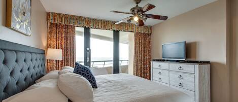 Een hotelkamer met een groot bed, een plafondventilator, een televisie en uitzicht op de oceaan.