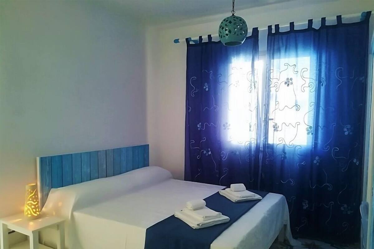 Una habitación de hotel con cama, mesita de noche y ventana con cortinas.