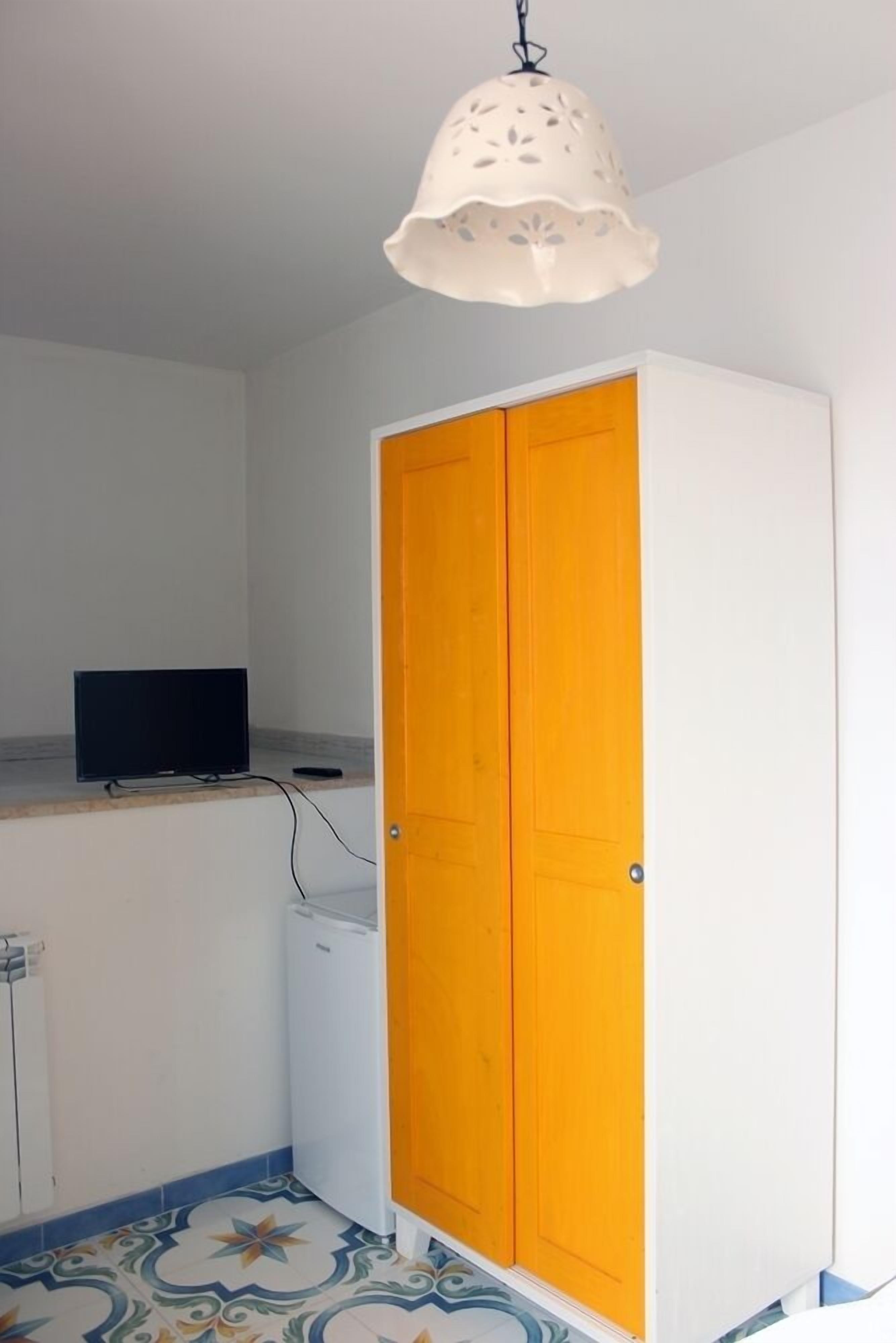 A room with a white wardrobe, a small white appliance, a television on a counter, and a patterned floor.