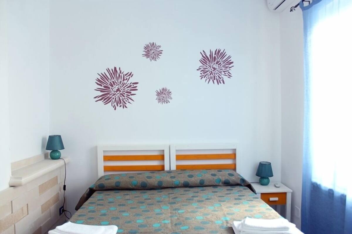 Una habitación de hotel con una cama, dos mesitas de noche, aire acondicionado montado en la pared y decoración en la pared.