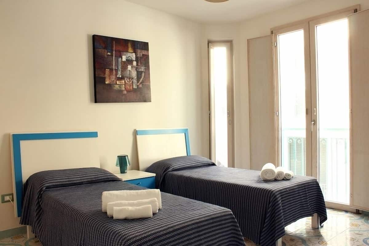 A hotel room with two beds, a painting on the wall, and a balcony with a view.