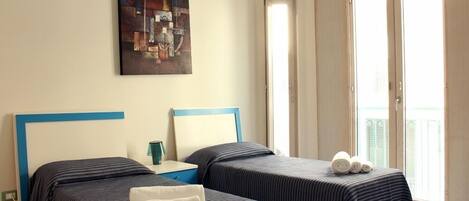 A hotel room with two beds, a painting on the wall, and a balcony with a view.