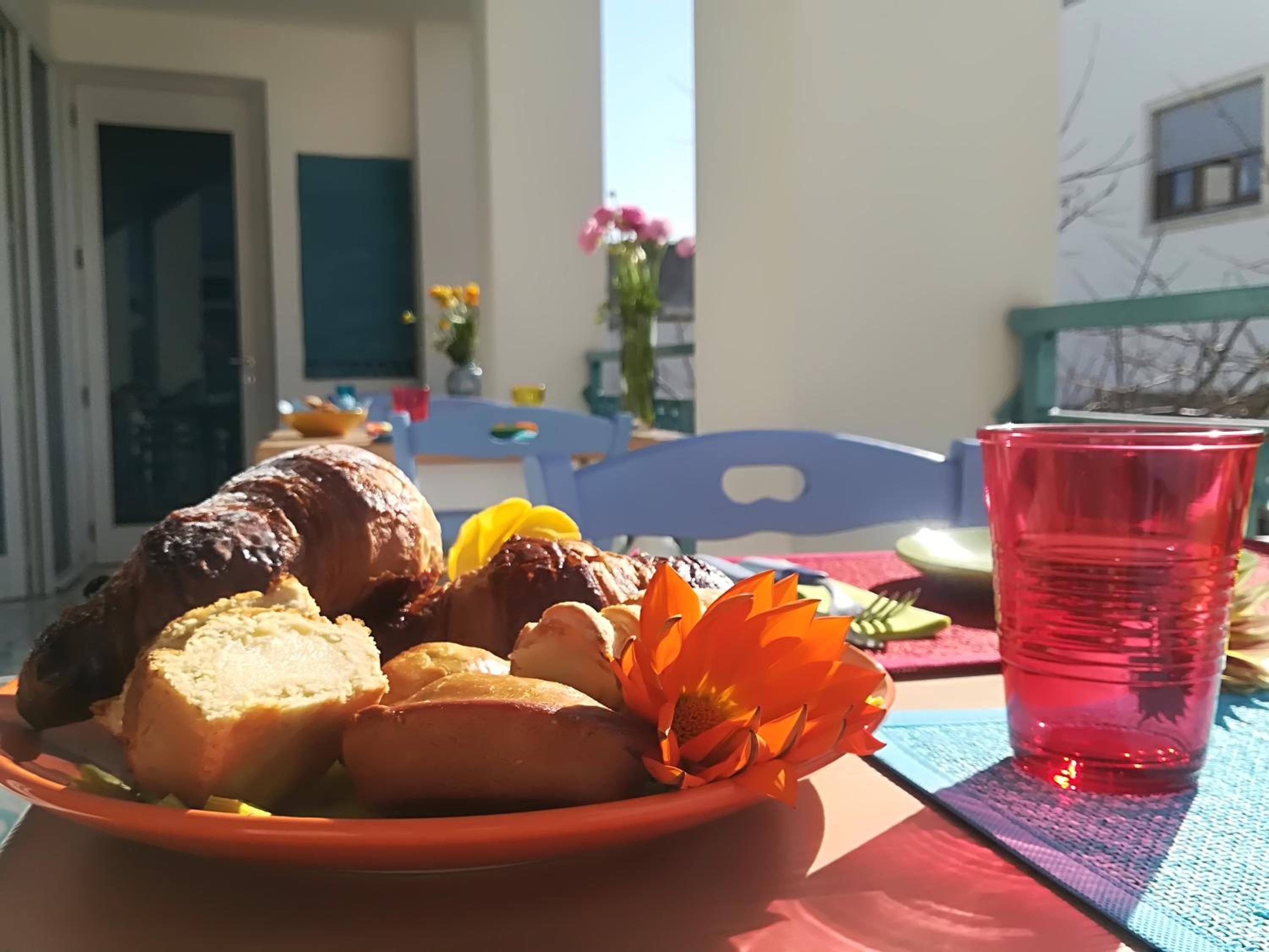 Uma mesa com um prato de comida, uma caneca vermelha e uma flor.
