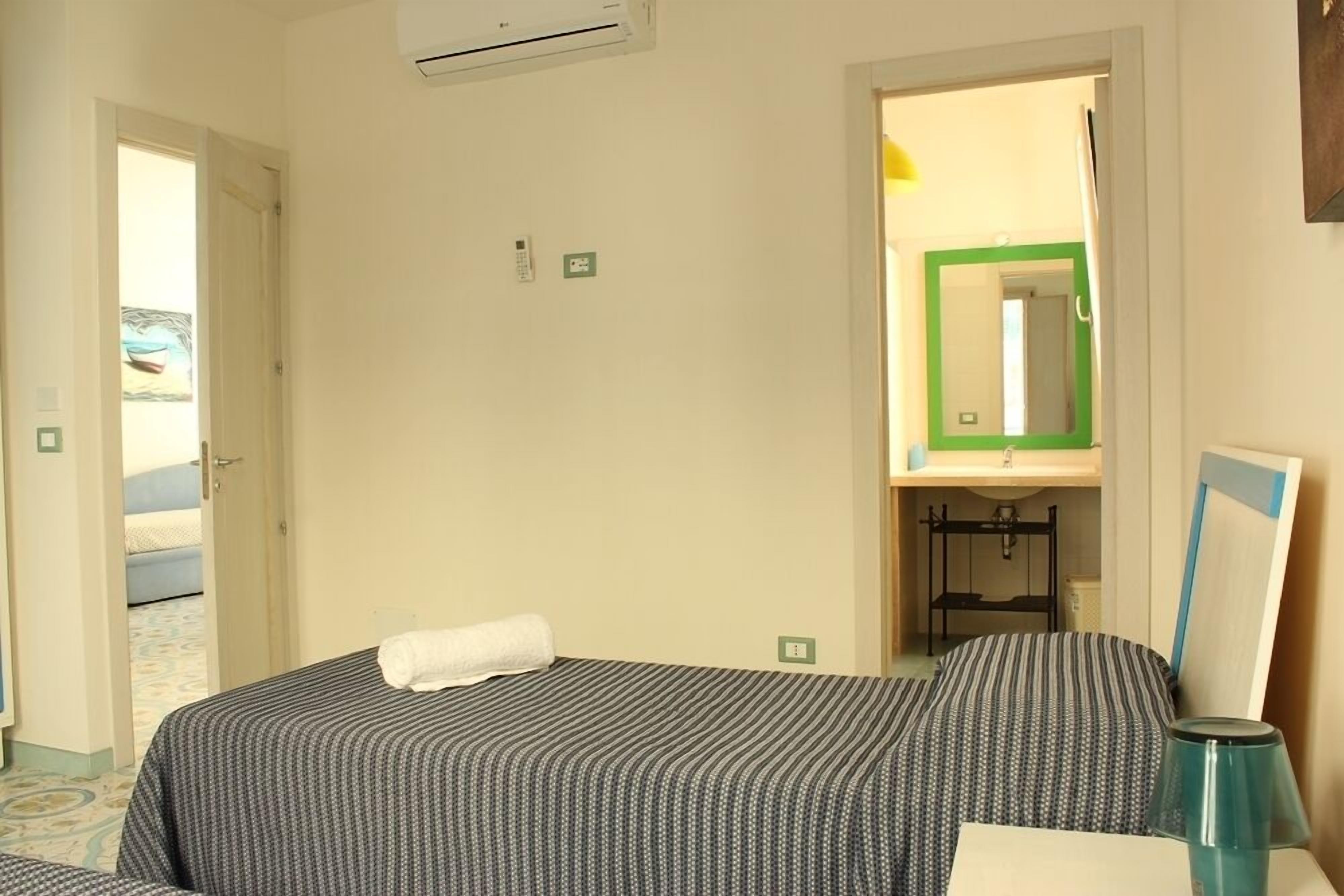 Een hotelkamer met een bed, nachtkastje, lamp en een badkamer die door een open deur zichtbaar is.