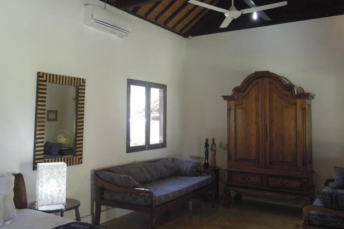 A room with a bed, a sofa, a wooden cabinet, a ceiling fan, and a window.