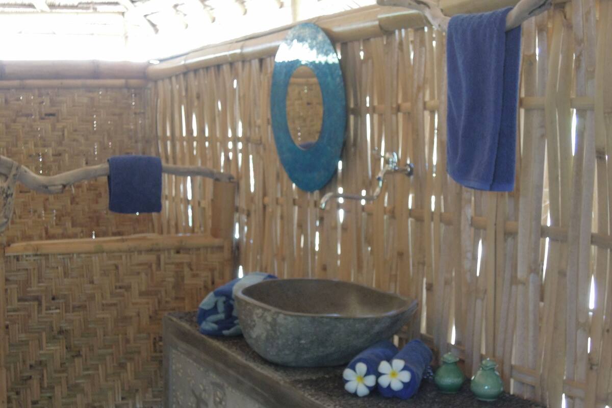 A rustic bathroom with a woven bamboo wall, a large basin, and a blue towel hanging on a rack.