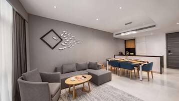 Una sala moderna con un sofá seccional gris, una mesa redonda y un comedor con sillas azules y una mesa de madera.