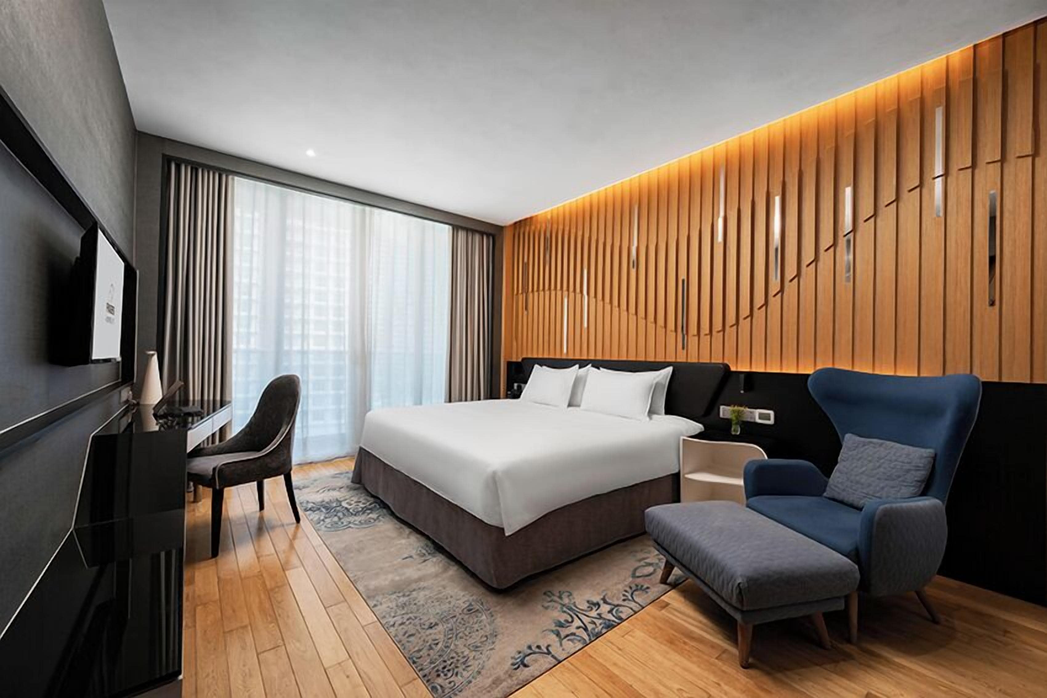 A modern hotel room with a large bed, a desk, a chair, and a TV.
