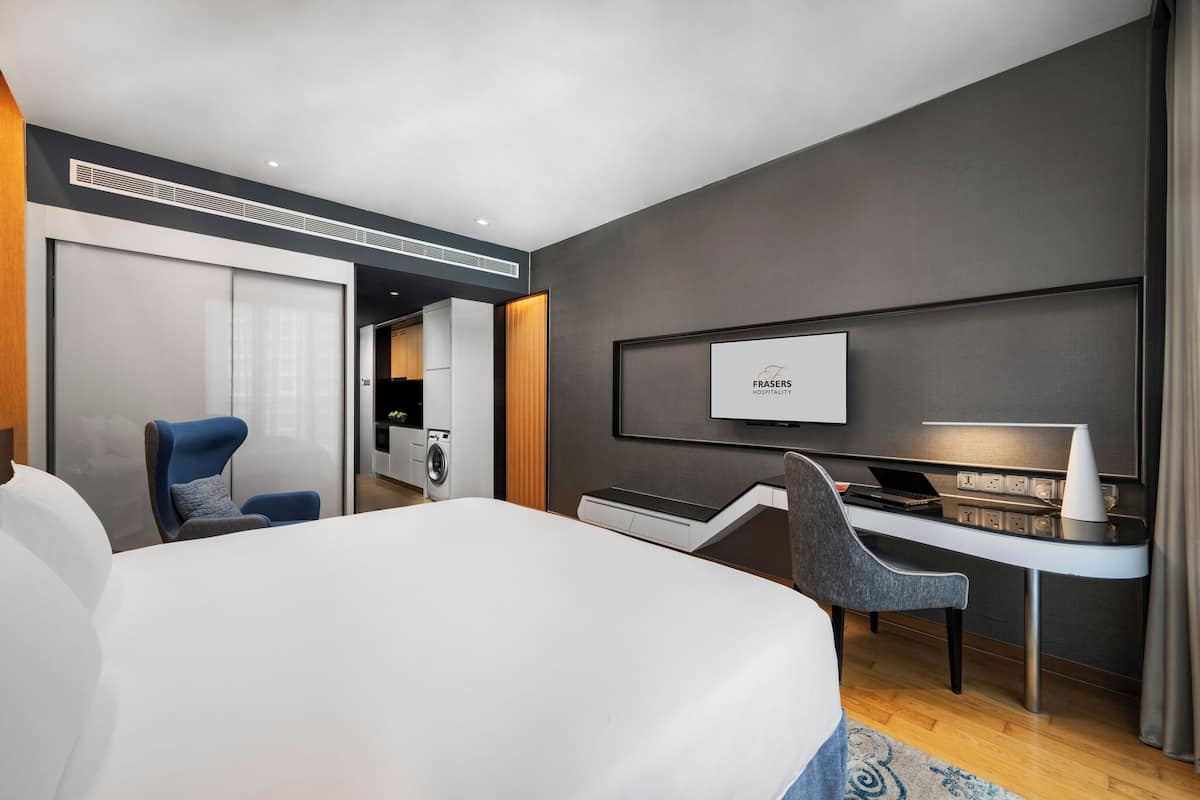 A modern hotel room with a large bed, a desk with a laptop, a TV, and a chair.