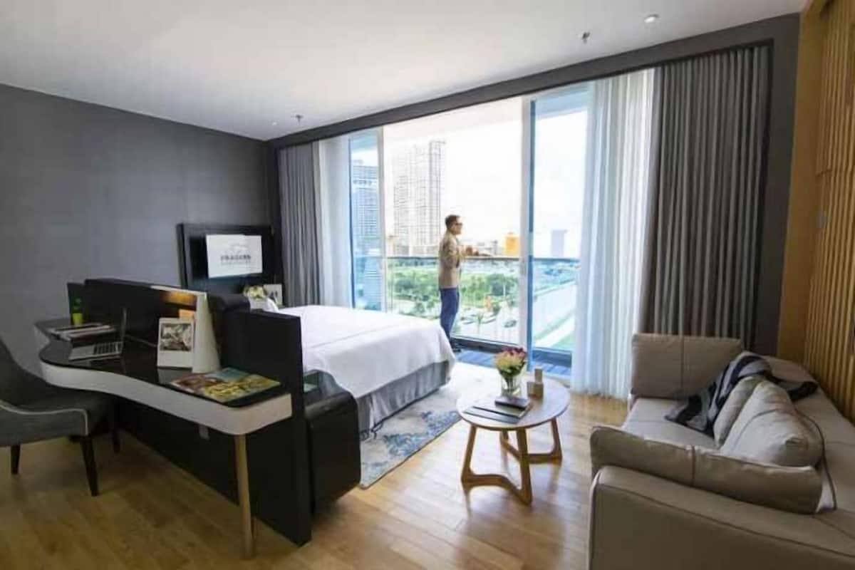 A modern hotel room with a bed, a desk, a sofa, and a balcony with a city view.