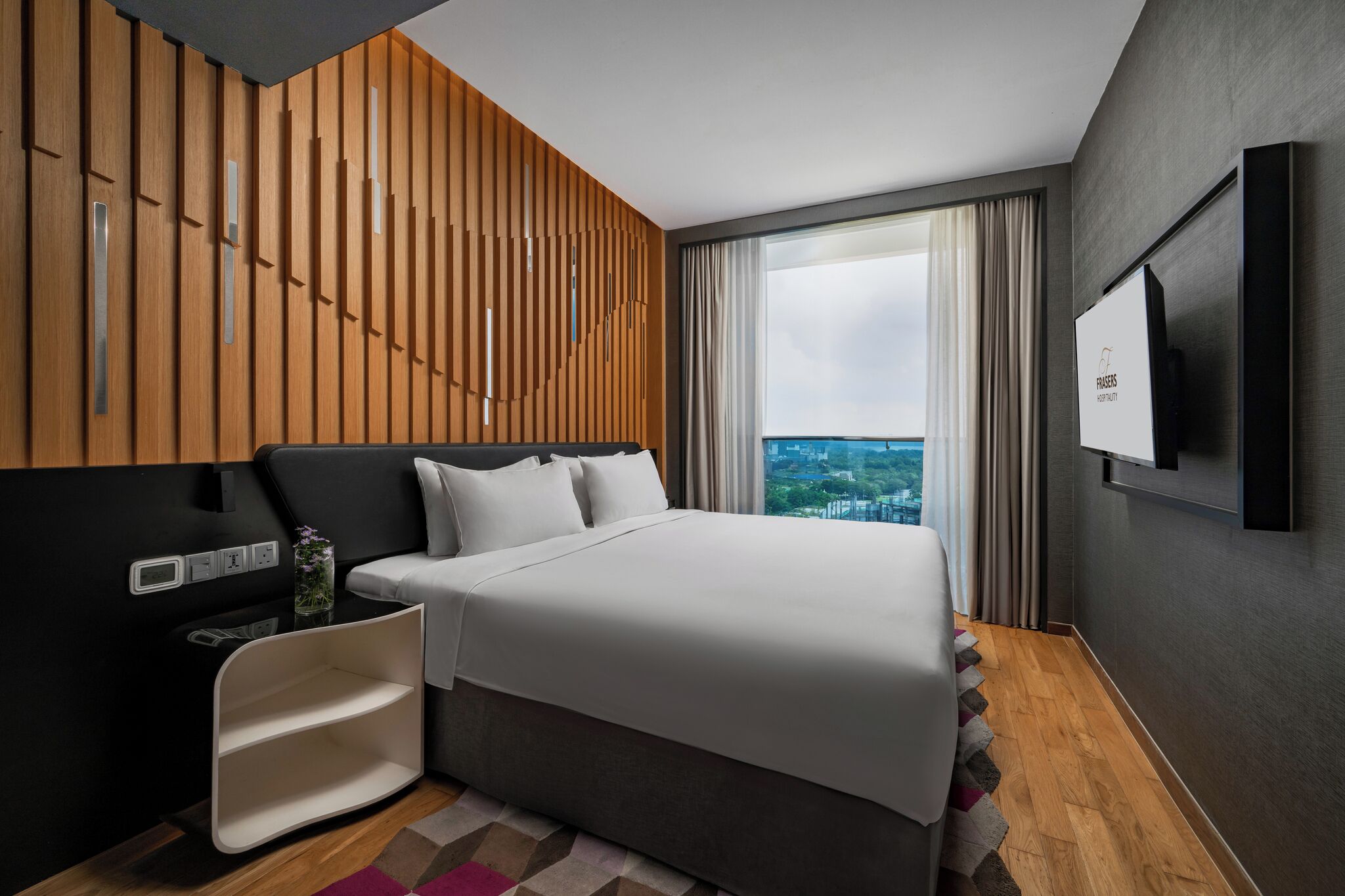 Ein modernes Hotelzimmer mit einem großen Bett, einem an der Wand montierten Fernseher und Blick auf die Stadt.