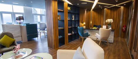 A modern hotel lobby with a sofa, armchairs, a coffee table, and a bookshelf.