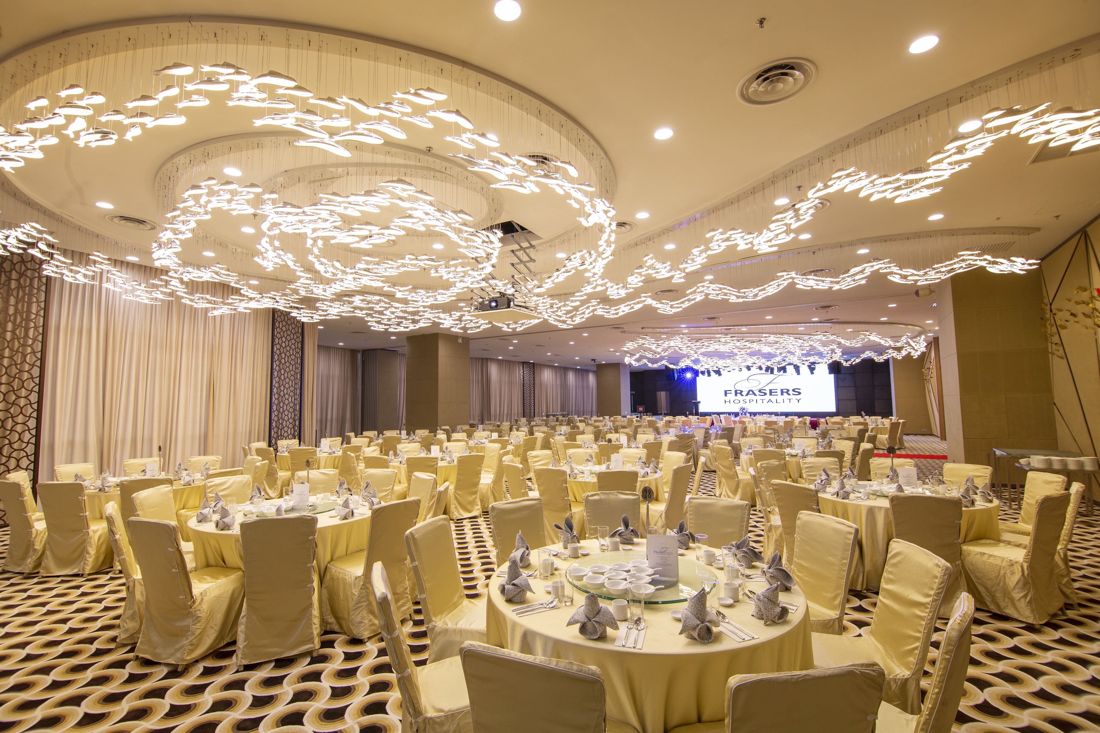 A banquet hall with round tables, chairs, and a stage with a screen.