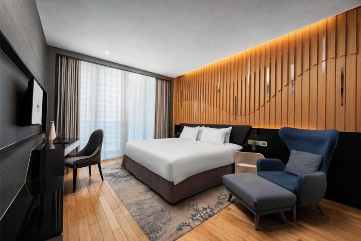 A modern hotel room with a large bed, a desk, a chair, and a sofa.