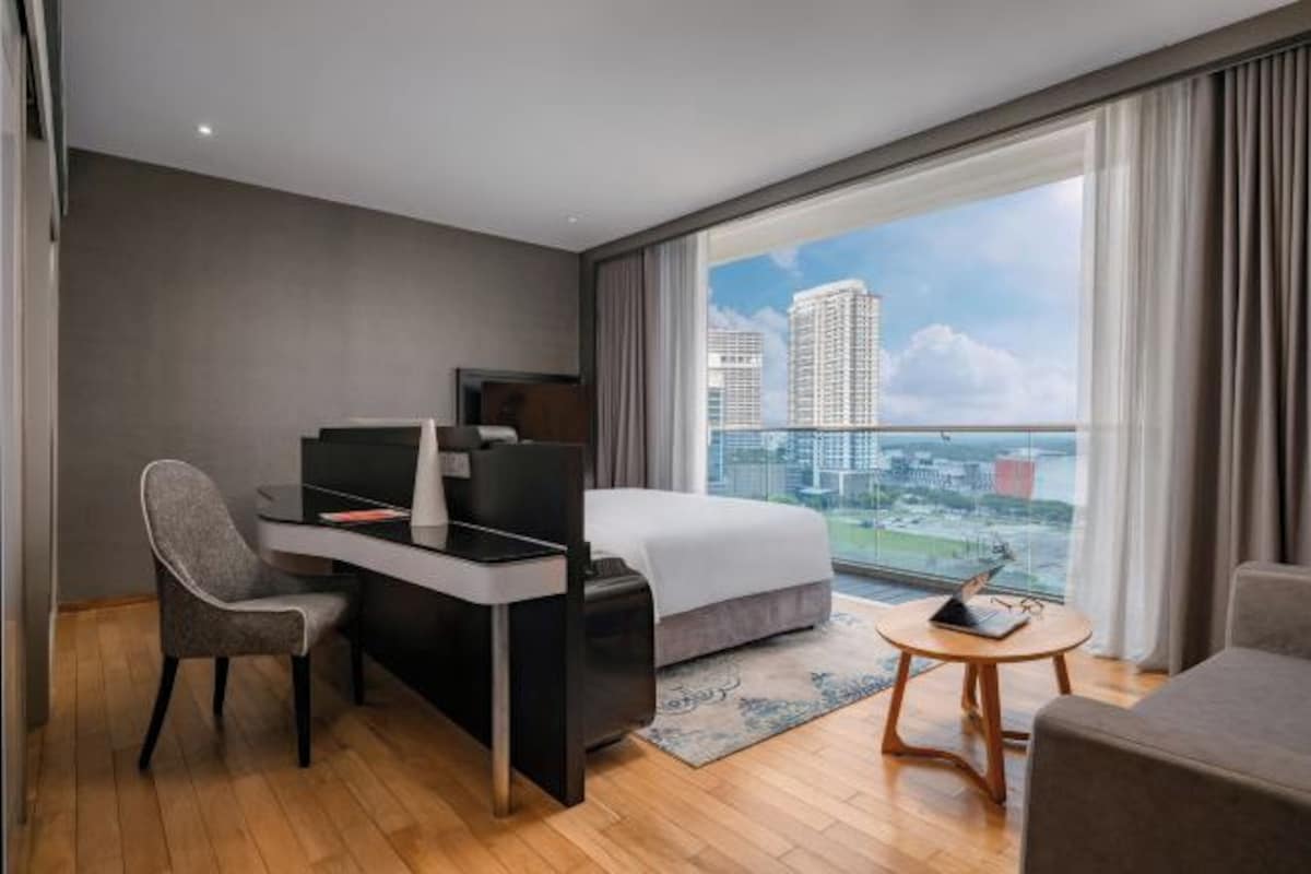 A modern hotel room with a bed, desk, chair, and a view of the cityscape.