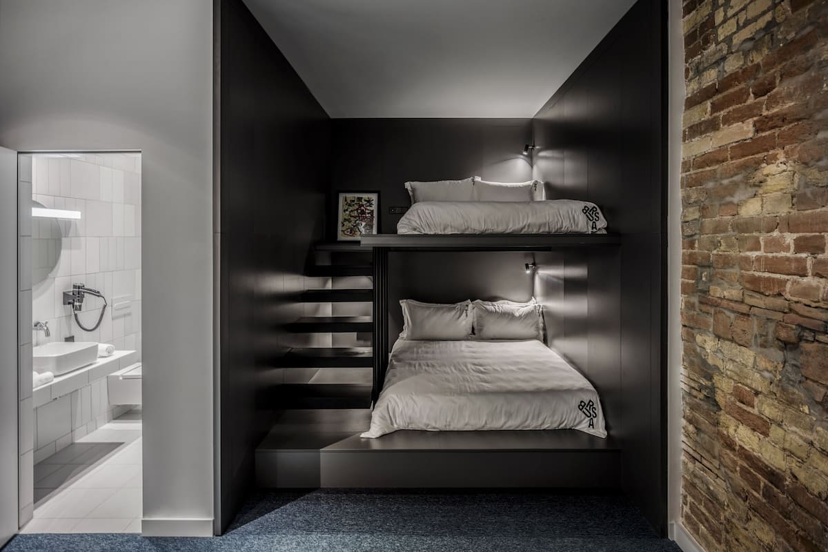 A compact room with a bunk bed, a small bathroom with a shower, and a brick wall.