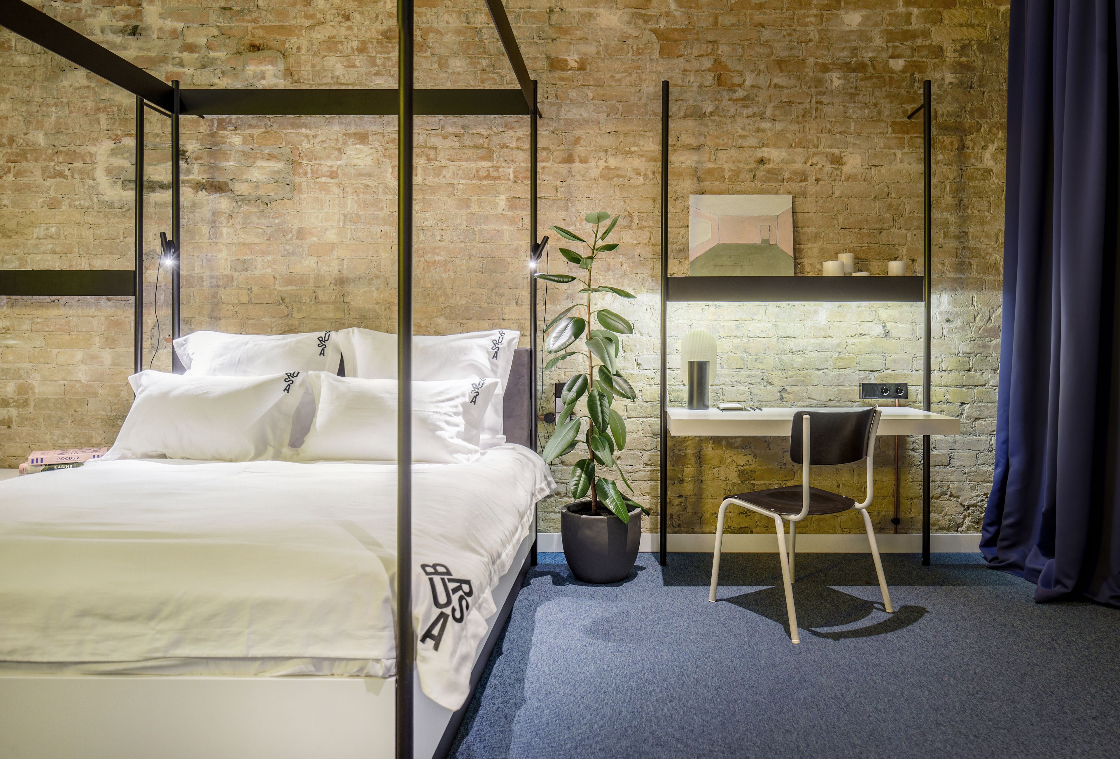 Una habitación de hotel moderna con una cama con dosel, un escritorio con silla y una planta en maceta.