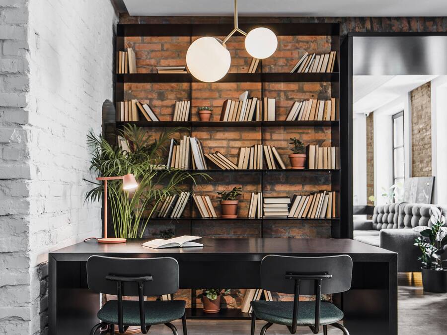 A modern dining area with a brick wall bookshelf, two black chairs, and a round pendant light.