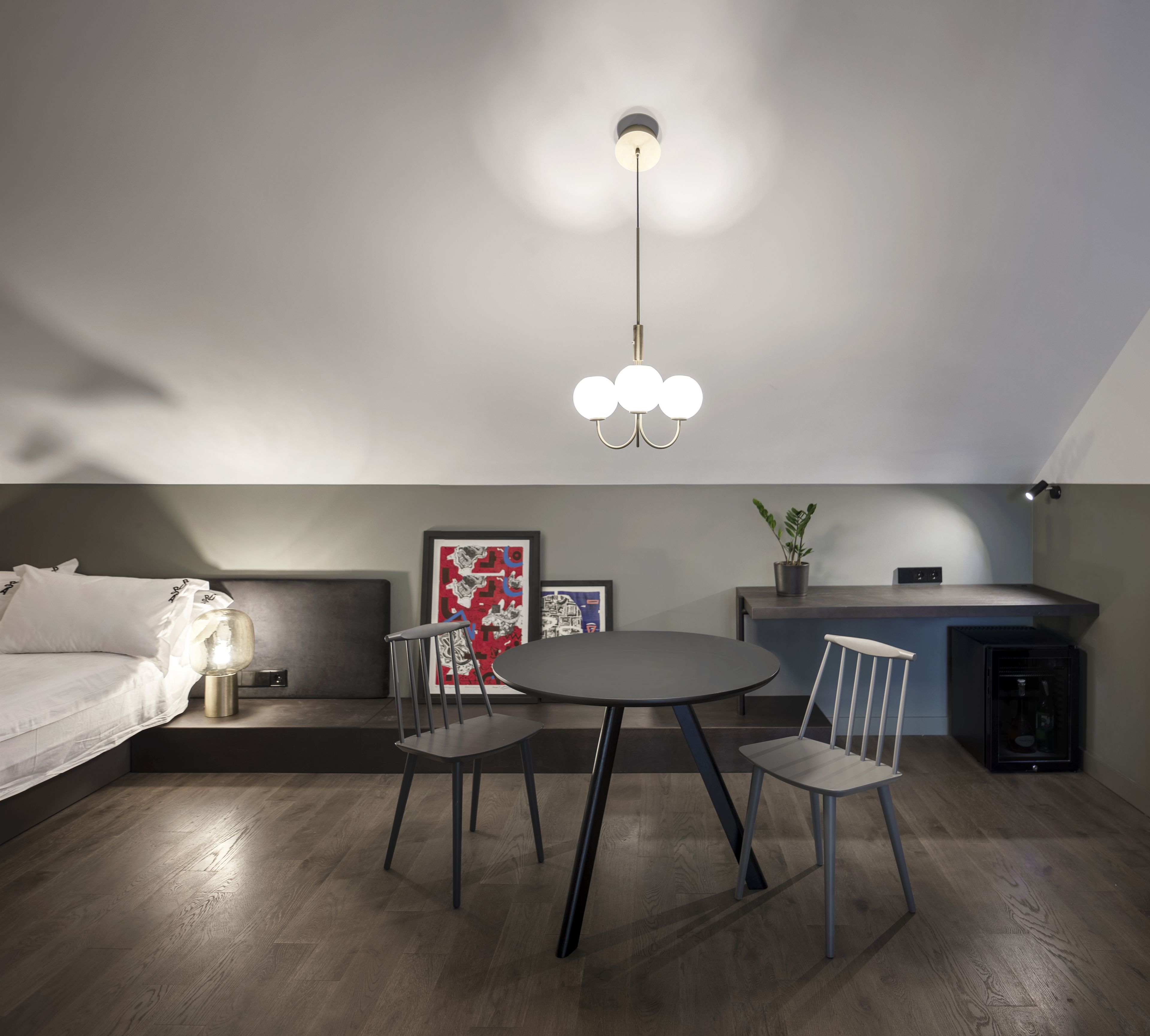 Un dormitorio moderno con cama, mesita de noche, lámpara y un rincón comedor con sillas y mesa.