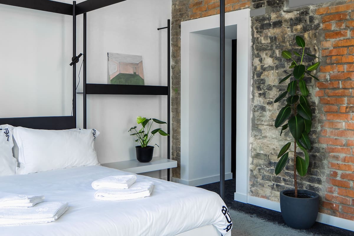 A modern hotel room with a large bed, a potted plant, and exposed brick walls.