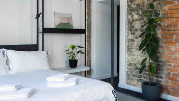 Una habitación de hotel moderna con una cama grande, una planta en maceta y paredes de ladrillo visto.