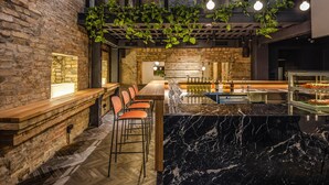 A modern bar area with a marble countertop, wooden bar stools, and a brick wall backdrop. - BURSA Hotel Kyiv (Kyiv)