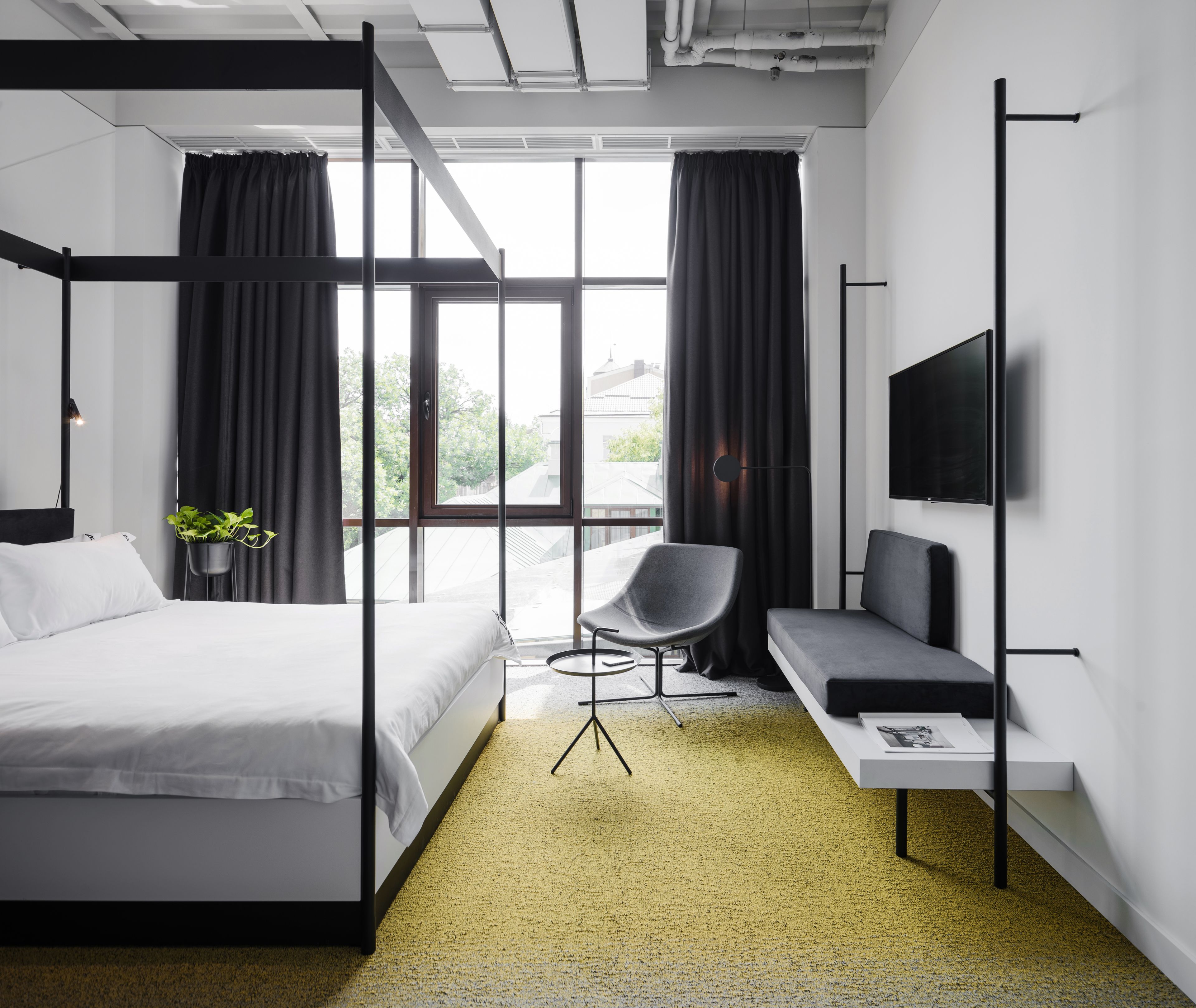 Una habitación de hotel moderna con una cama grande, un escritorio, una silla, un televisor y un ventanal con cortinas.