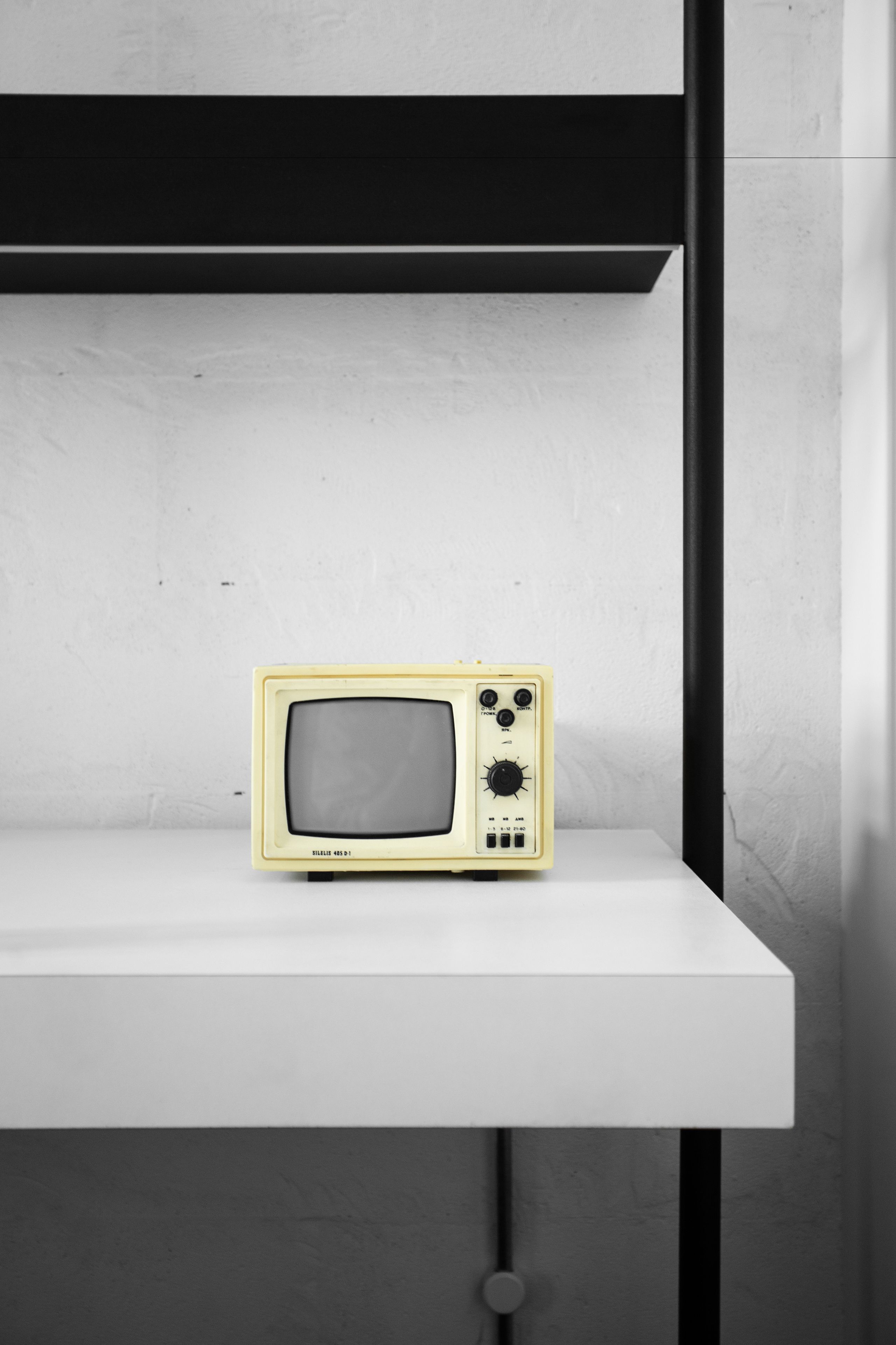 Un televisor antiguo sobre un estante blanco frente a una pared con textura.