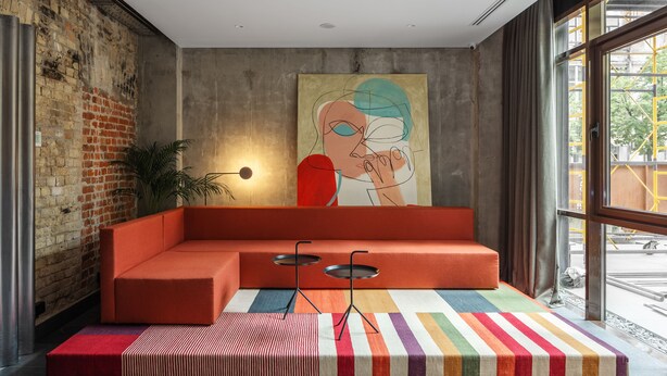 A modern room with a sectional sofa, a colorful striped rug, a minimalist table, and a large abstract painting on the wall. - BURSA Hotel Kyiv (Kyiv)