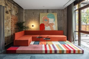 A modern room with a sectional sofa, a colorful striped rug, a minimalist table, and a large abstract painting on the wall. - BURSA Hotel Kyiv (Kyiv)