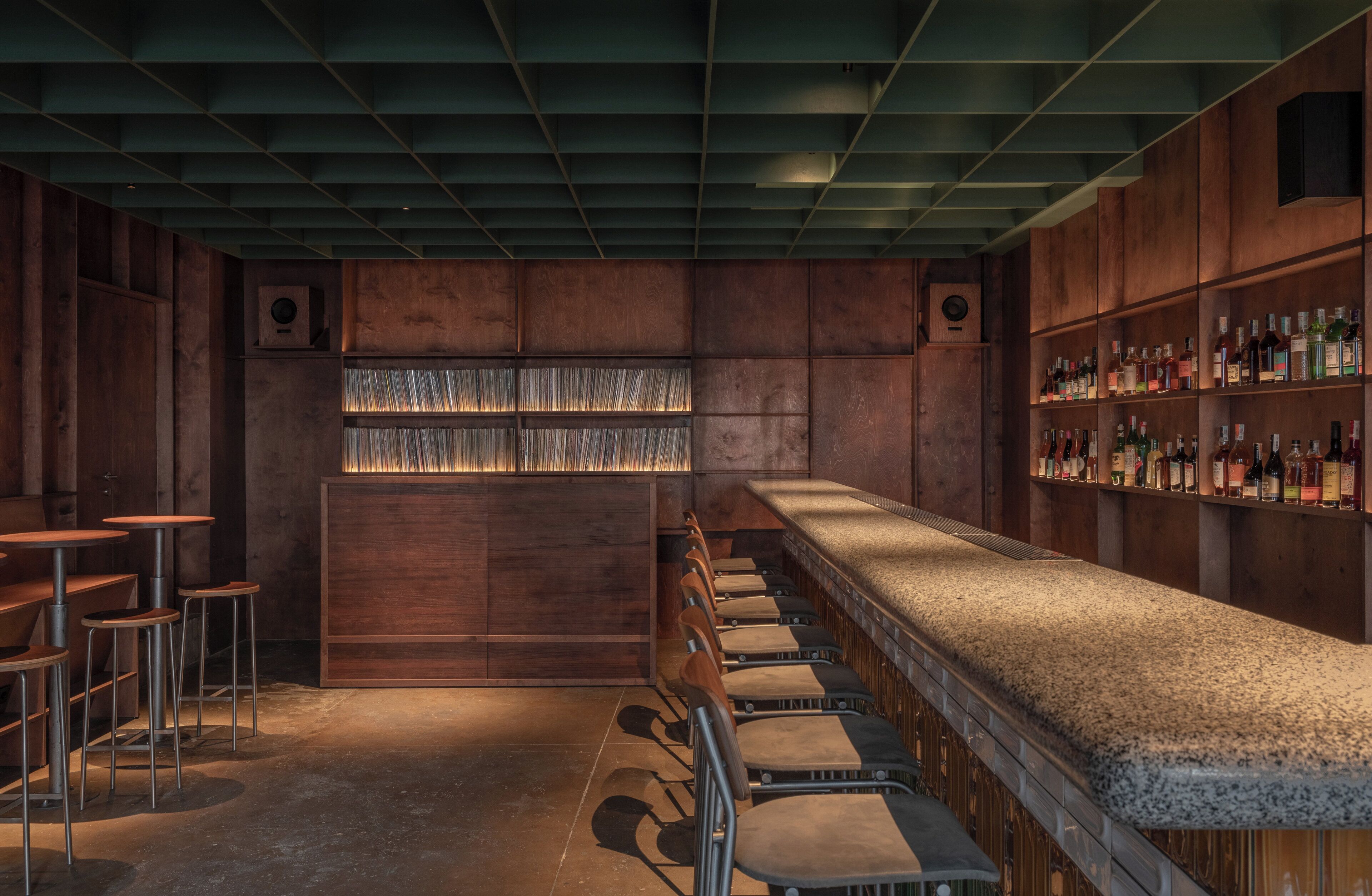 A bar area with wooden paneling, a long counter, and multiple stools.