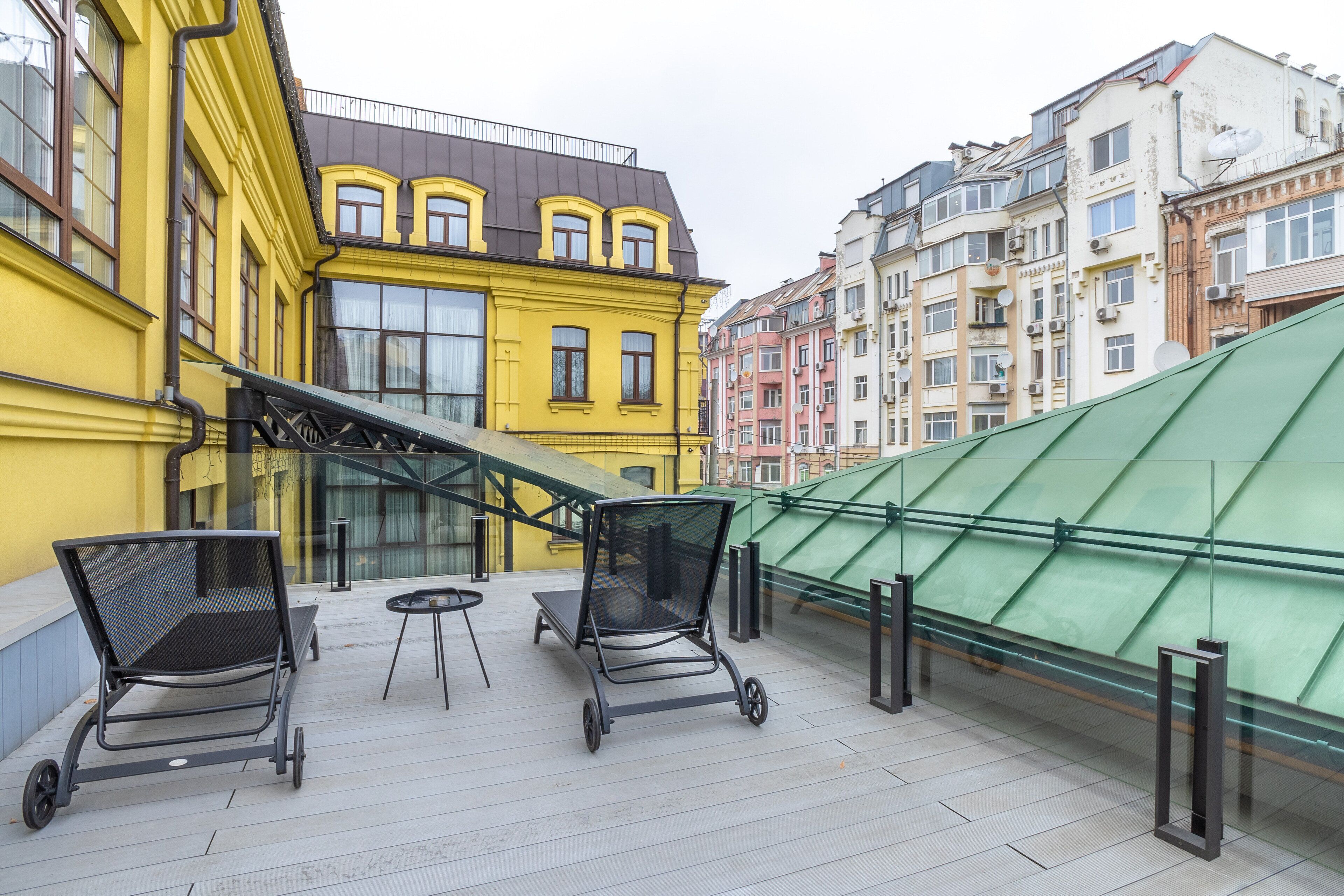 A rooftop terrace with two lounge chairs, a small table, and a glass railing.