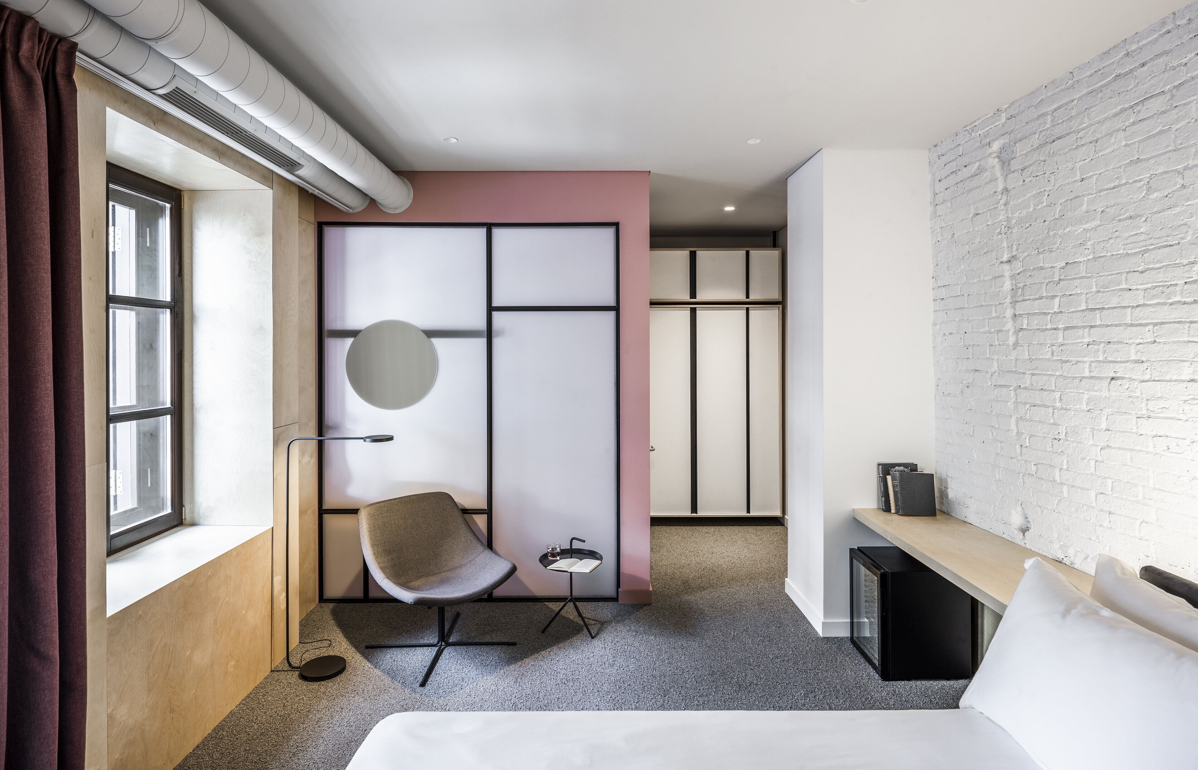 Een moderne hotelkamer met een bed, een bureau, een stoel en een groot raam.
