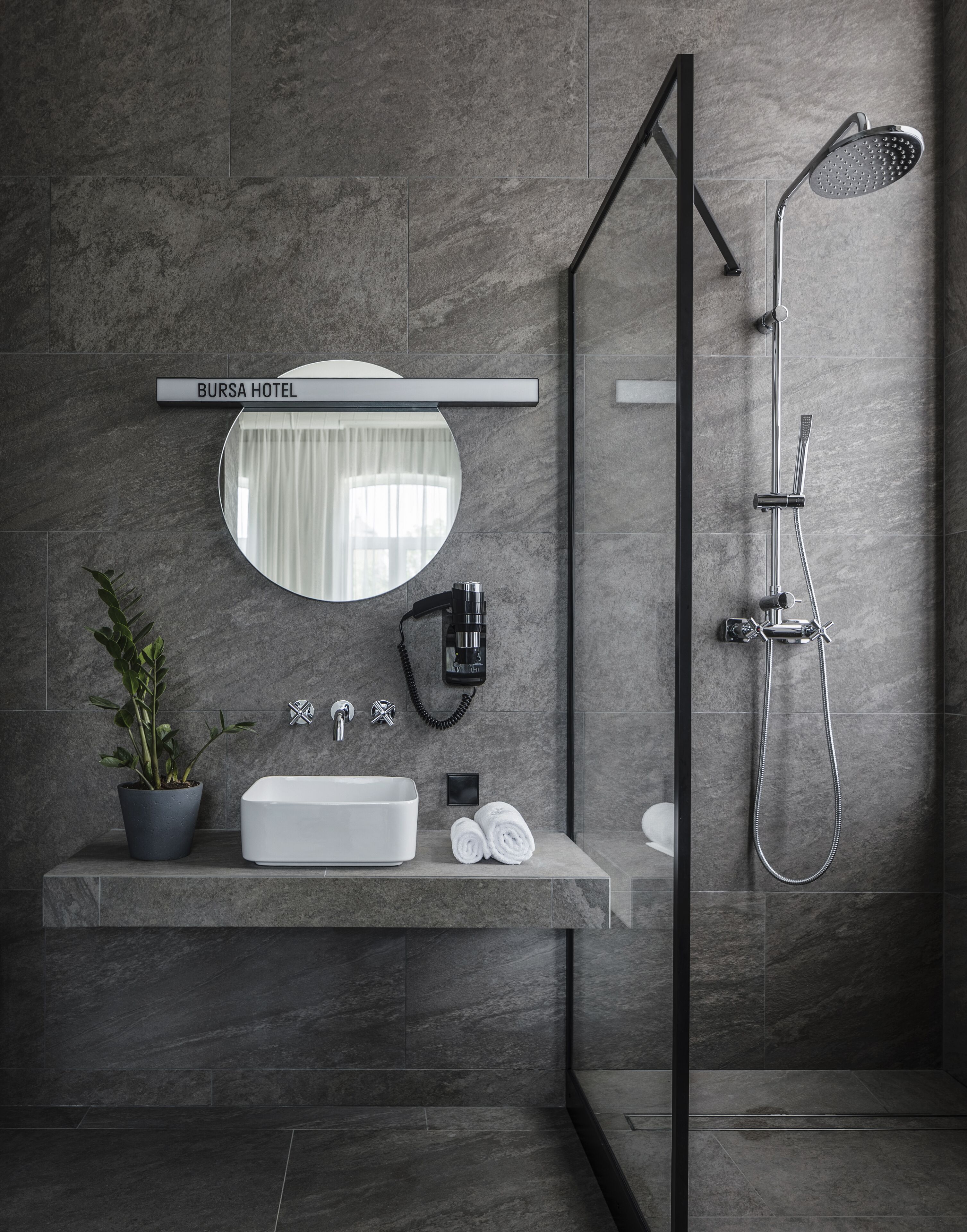 A modern bathroom with a large mirror, a sink, a shower, and a potted plant.