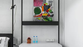 Una stanza moderna e accogliente con un letto a castello, una scrivania bianca con due bottiglie, un quadro astratto dai colori vivaci e un pouf grigio.