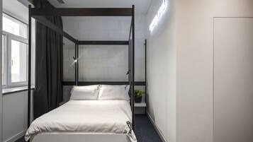 A modern bedroom with a four-poster bed, a potted plant, and a bright ceiling light.