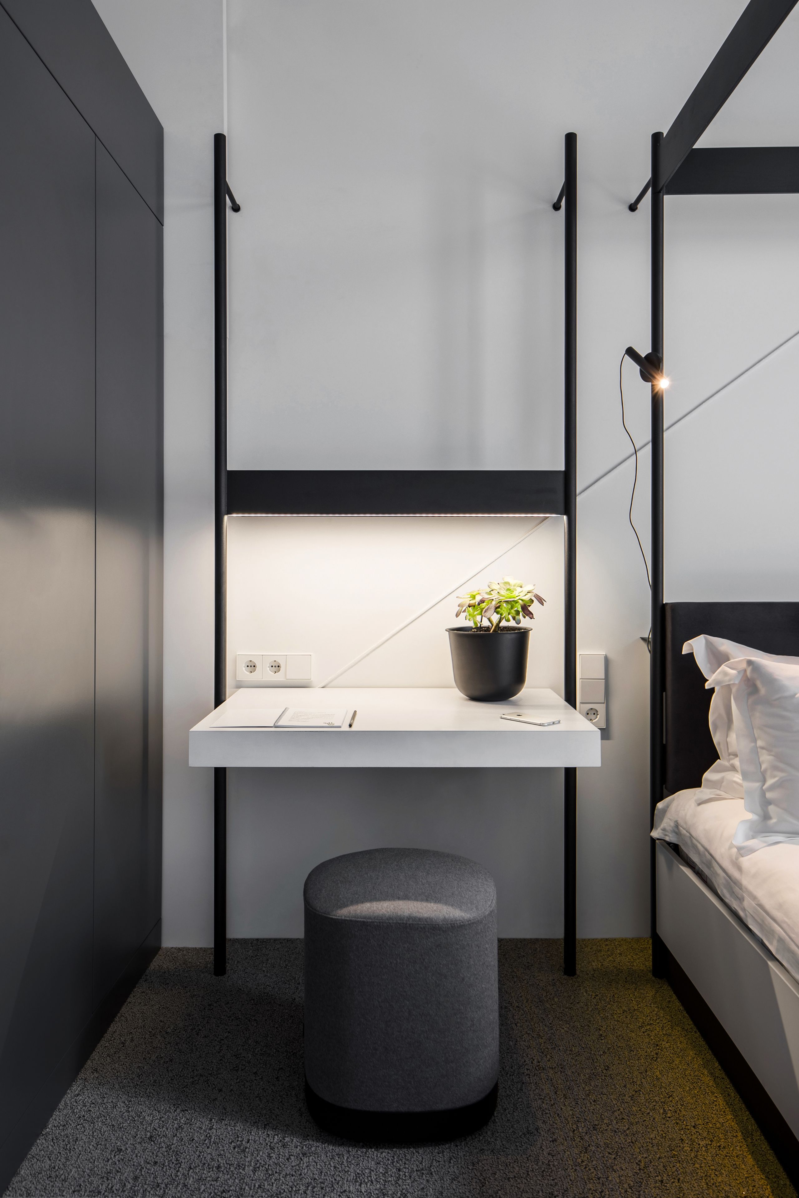 Un dormitorio compacto con una cama litera, una mesita de noche con una planta en maceta y un taburete pequeño.