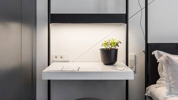 Un dormitorio compacto con una cama litera, una mesita de noche con una planta en maceta y un taburete pequeño.