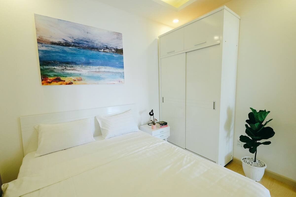Ein Schlafzimmer mit Bett, Nachttisch, Topfpflanze, Kleiderschrank und einem Bild an der Wand.