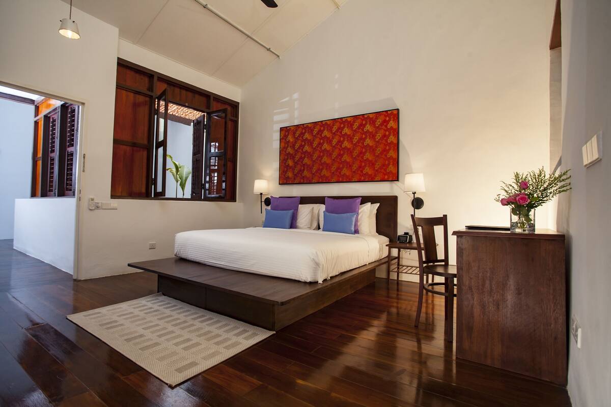 Une chambre à coucher moderne avec un grand lit, un plancher en bois, un petit bureau et une peinture abstraite aux couleurs vives.