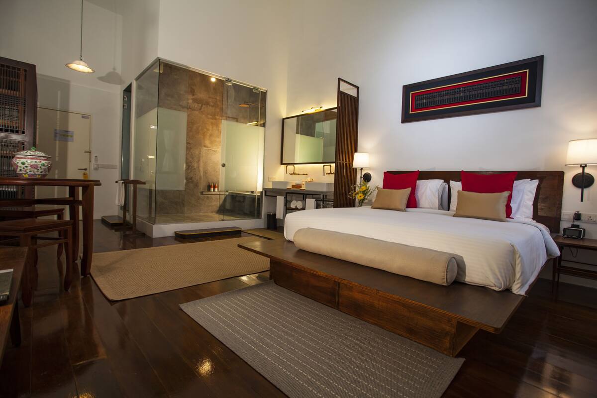 Une chambre d’hôtel moderne dotée d’un grand lit, d’une douche en verre, d’un bureau en bois et d’un grand miroir.