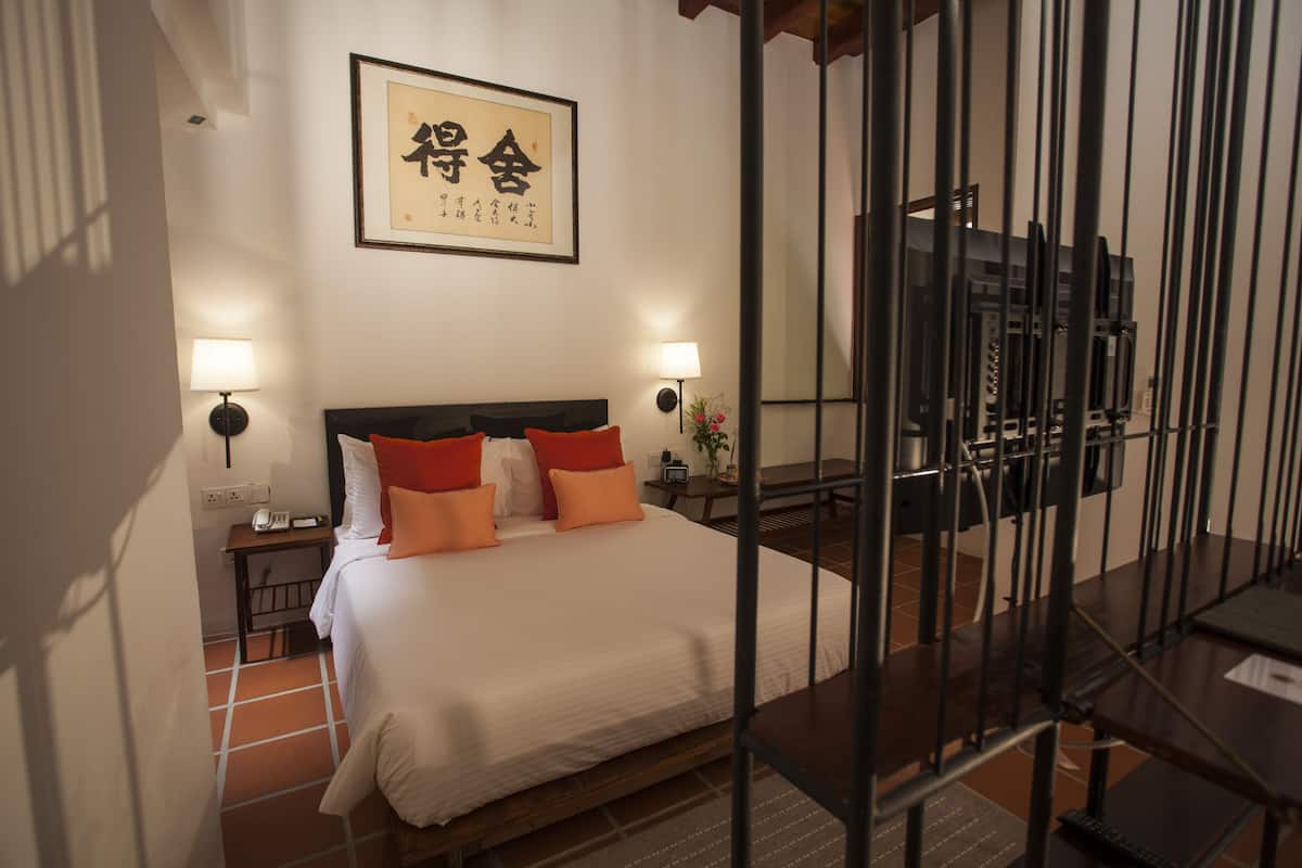 Une chambre d’hôtel avec un lit, deux lampes de chevet, une table de nuit, une œuvre d’art encadrée au mur et une vue sur l’extérieur par une fenêtre.