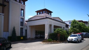 A building with a central entrance, a driveway, and parked cars. - Paradise Gardens & Dunes Hotel (Sozopol)