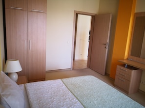 A bedroom with a bed, a nightstand, a lamp, a wardrobe, and a mirror.