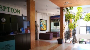 A reception area with a reception desk, a clock, a statue, a colorful painting, and a potted plant. - Paradise Gardens & Dunes Hotel (Sozopol)